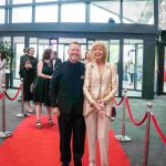 Two people standing on a red carpet and smiling