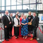 Eight people standing on a red carpet and smiling