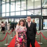 Two people standing on a red carpet and smiling