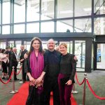 Three people standing on a red carpet and smiling