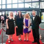 Four people standing on a red carpet and smiling