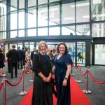 Two people standing on a red carpet and smiling