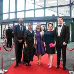 Five people standing on a red carpet and smiling