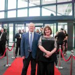 Two people standing on a red carpet and smiling