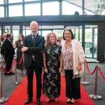 Three people standing on a red carpet and smiling