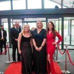 Three people standing on a red carpet and smiling