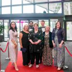 Seven people standing on a red carpet and smiling