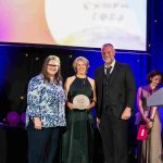 Actor Julian Lewis Jones and Chairs of Lighthouse Theatre and Theatr na nOg, smiling at the camera holding an award