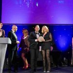 Two people from Port of Milford Haven standing on stage, holding an award and smiling at the camera