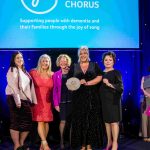 People from Cardiff & Vale Health Charity standing on stage with Grammy Award-winning Soprano Rebecca Evans, holding an award and smiling at the camera