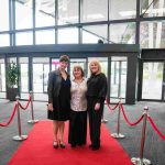 Three people standing on a red carpet and smiling