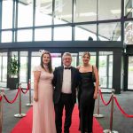 Three people standing on a red carpet and smiling