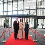 Three people standing on a red carpet and smiling