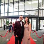 Two people standing on a red carpet and smiling